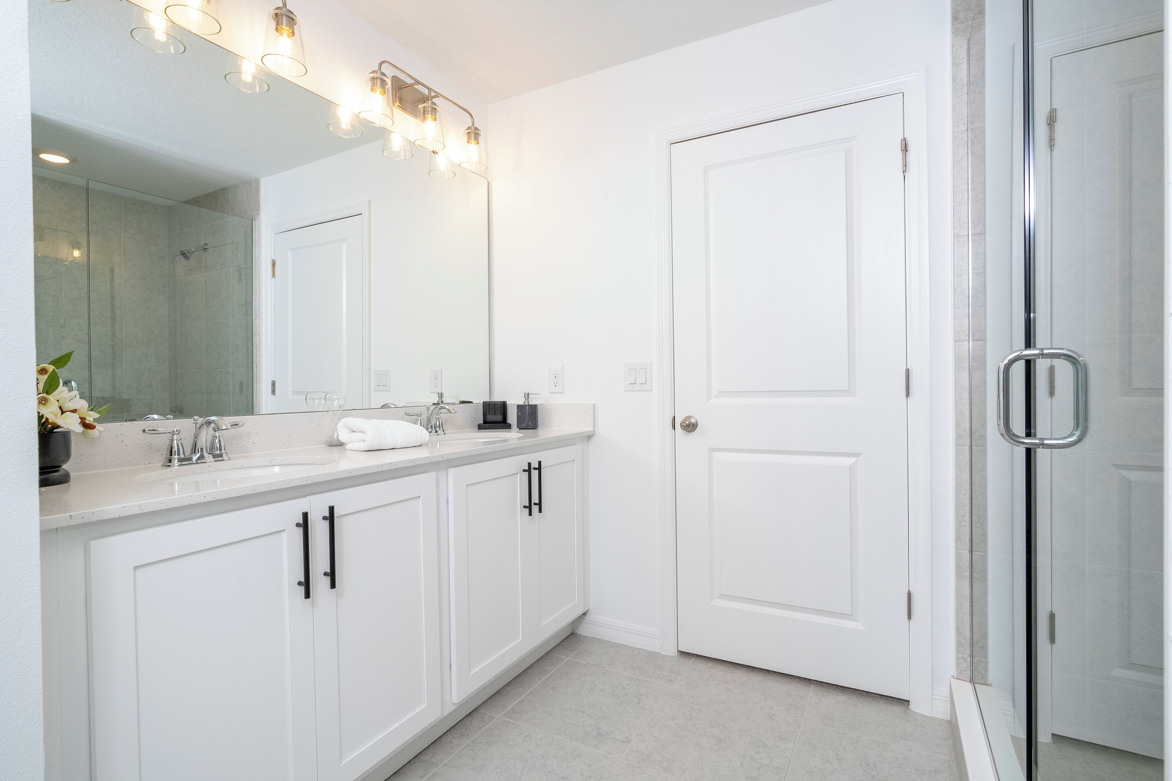 A modern bathroom with white cabinetry, a large mirror, and a glass shower enclosure.