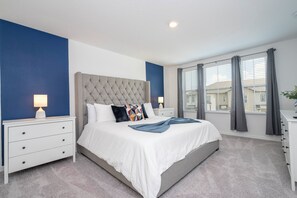 A bedroom with a large bed, two bedside tables, a nightstand, a window with curtains, and a view of buildings outside. - Gorgeous 3Bd Close To Disney @ Festival Resort 661 (Davenport)