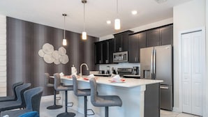 A modern kitchen with dark cabinets, a stainless steel refrigerator, a microwave, and a bar area with stools. - Gorgeous 4Bd W/ Pool & Waterpark @ Storey Lake 4836M (Kissimmee)
