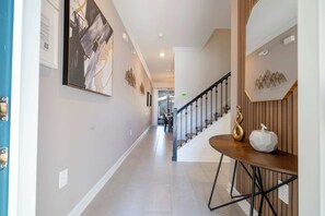 A hallway with a staircase, a dining area with a table and chairs, and a wall with framed artwork.
