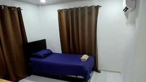 Une chambre avec deux lits, l’un recouvert d’une couvre-lit bleue et l’autre d’une couvre-lit jaune, et les deux sont garnis de serviettes. On y trouve également un ventilateur de plafond et un appareil de climatisation fixé au mur.