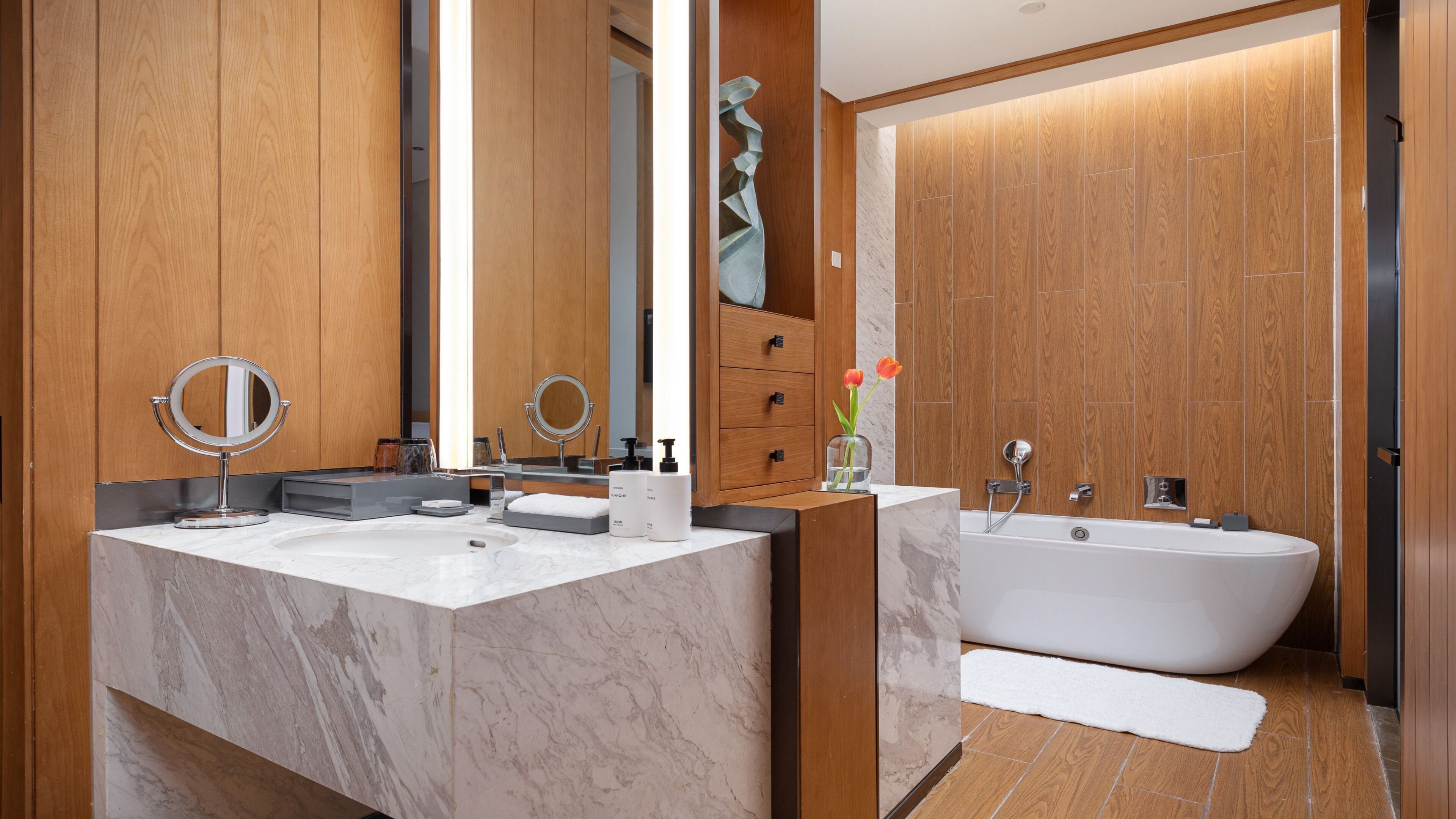 Un baño moderno con paneles de madera, un lavabo grande de mármol, una bañera independiente y dos espejos.