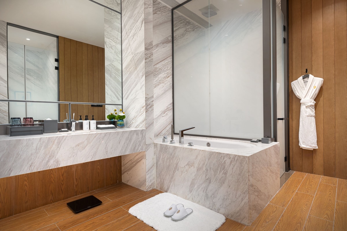 A modern bathroom with a marble vanity, a freestanding bathtub, and a wooden panel wall.