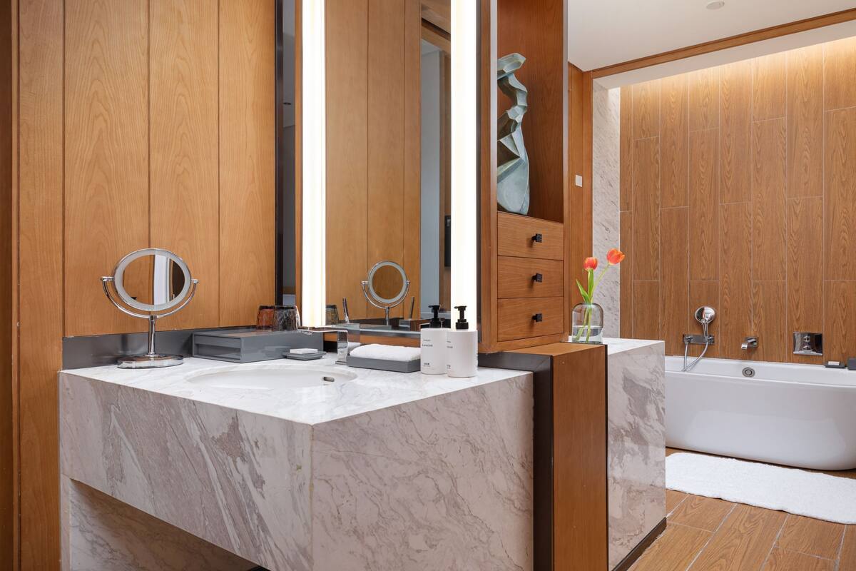 Une salle de bain moderne avec un lambris en bois, un grand lavabo en marbre, une baignoire sur pieds et deux miroirs.