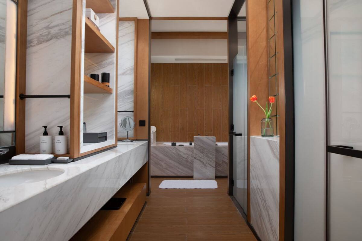Une salle de bain moderne avec un meuble-lavabo en marbre, des étagères en bois, un grand miroir et une cabine de douche en verre.