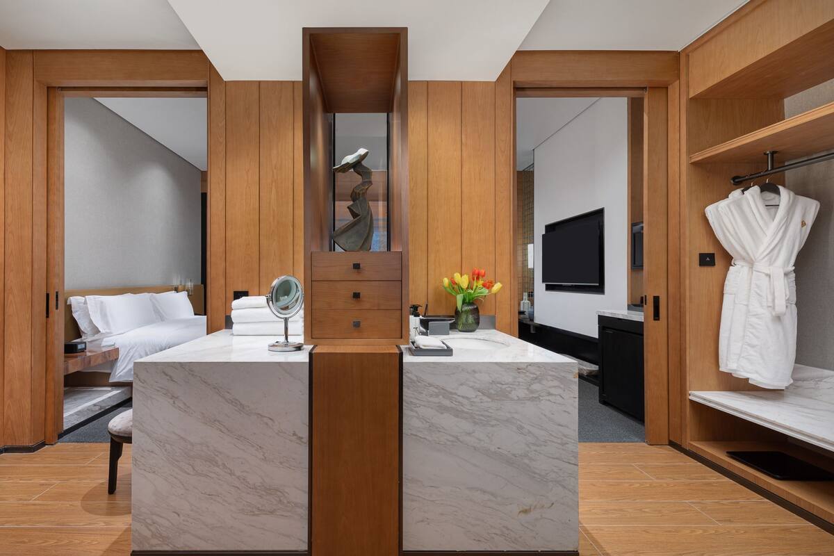 Une salle de bain moderne avec un meuble-lavabo en marbre, un grand miroir, un meuble en bois, une baignoire et un porte-peignoir.