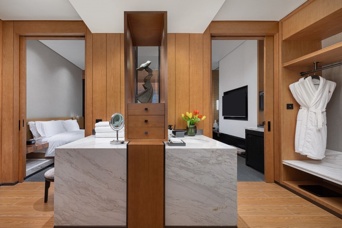 A modern bathroom with a marble vanity, a large mirror, a wooden cabinet, a bathtub, and a robe rack.