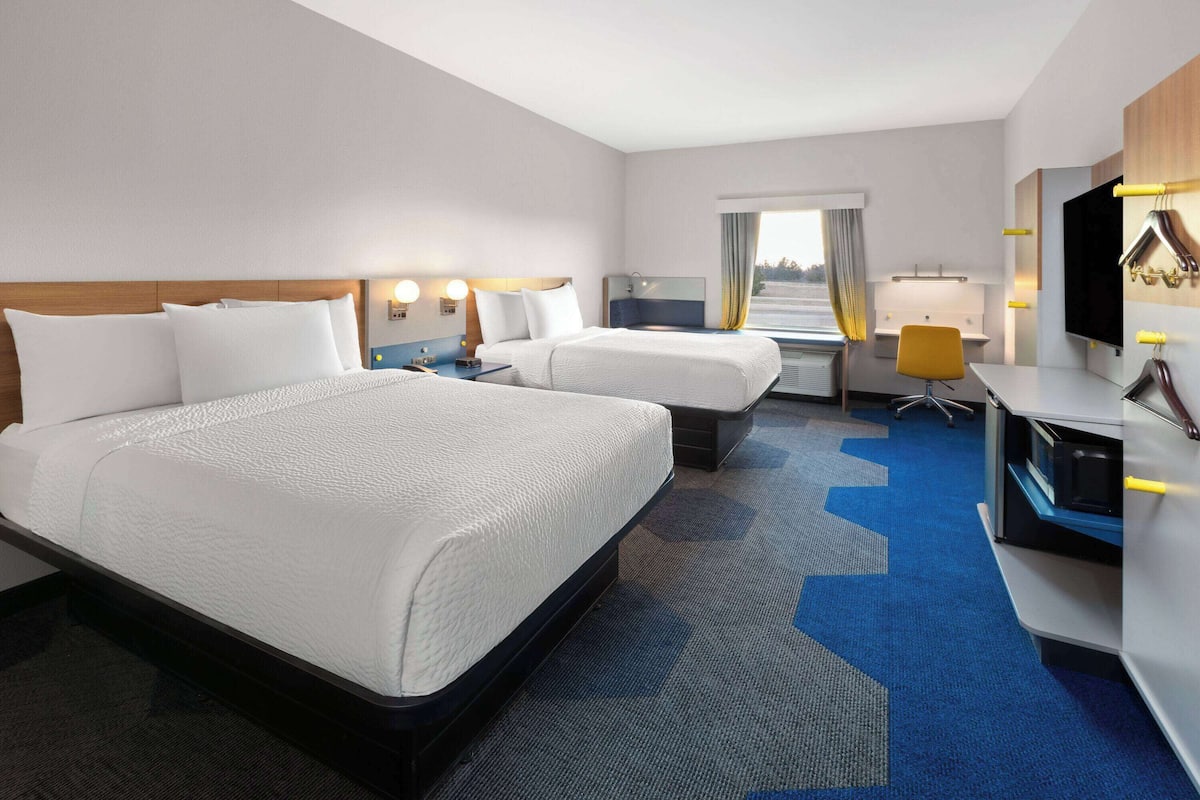 Une chambre d’hôtel avec deux lits, un bureau, une chaise, une télévision et une fenêtre avec des rideaux.