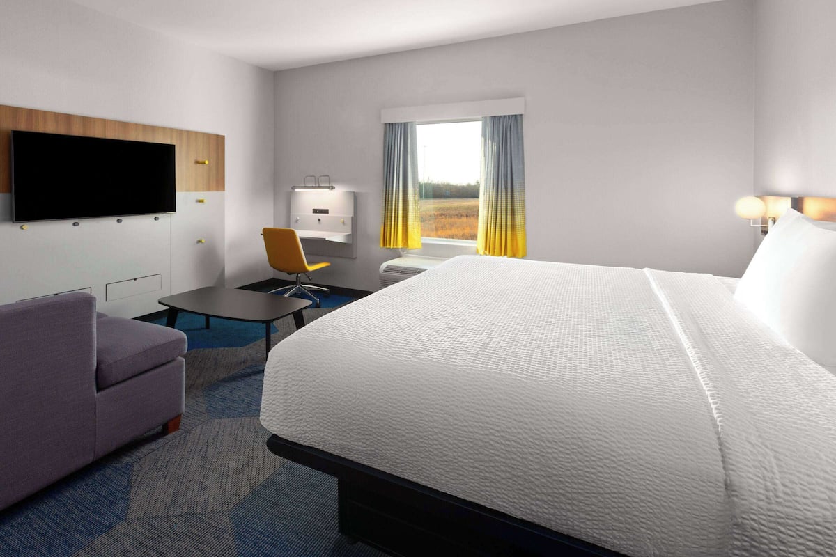 Une chambre d’hôtel dotée d’un grand lit, d’un bureau avec une chaise, d’un téléviseur à écran plat fixé au mur et d’une fenêtre avec des rideaux.