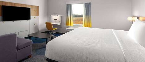 Habitación de hotel con una cama grande, un escritorio con silla, un televisor de pantalla plana en la pared y una ventana con cortinas.