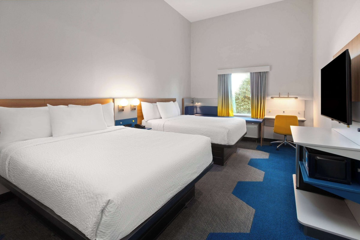 Une chambre d’hôtel avec deux lits, un bureau, une chaise, une télévision et une fenêtre avec des rideaux.