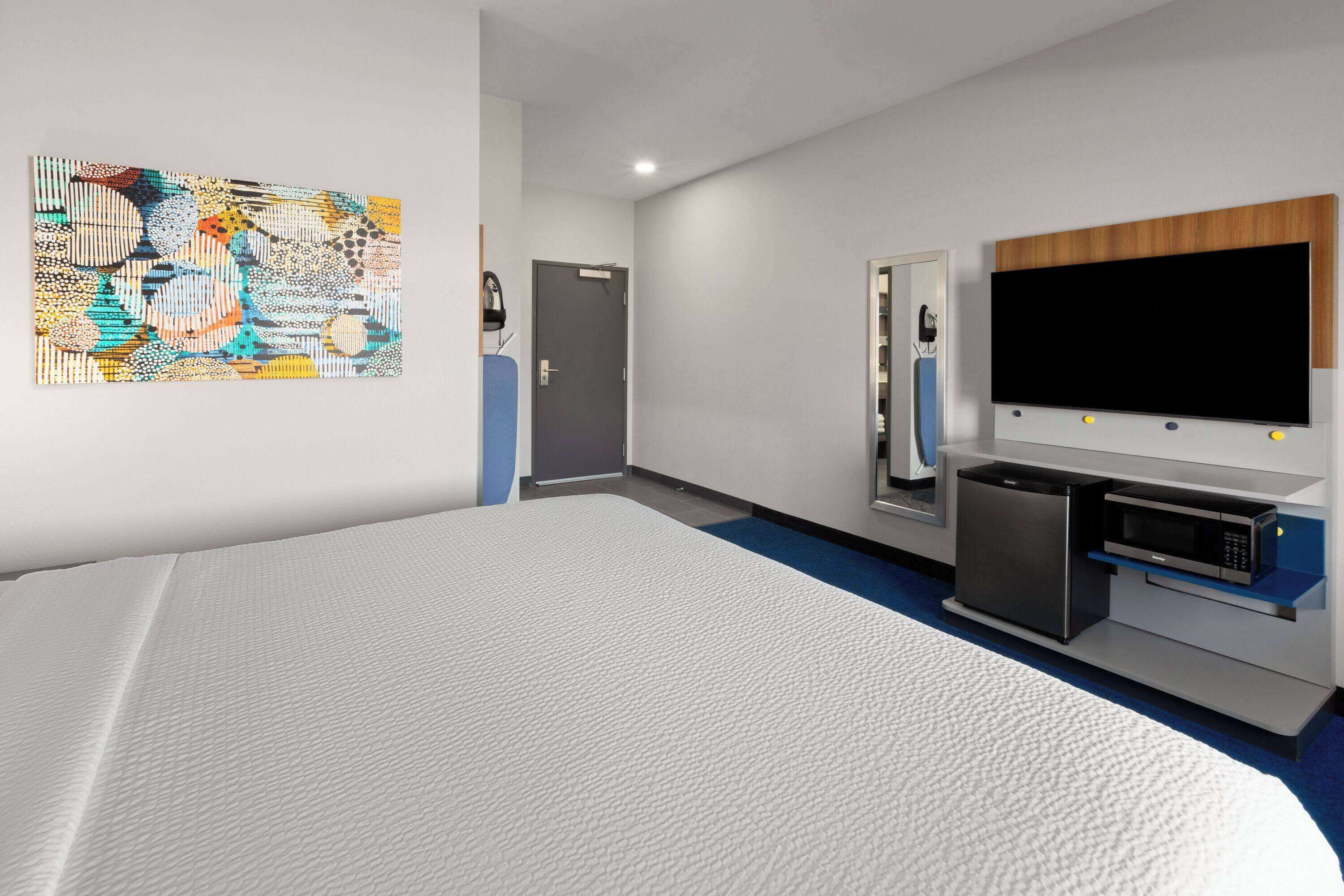 A modern hotel room with a large bed, a flat-screen TV, a microwave, and a small refrigerator.