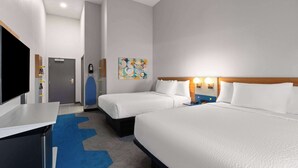 Ein Hotelzimmer mit zwei Betten, einem Schreibtisch, einem Fernseher, einem Gemälde an der Wand und einem blauen Teppich.