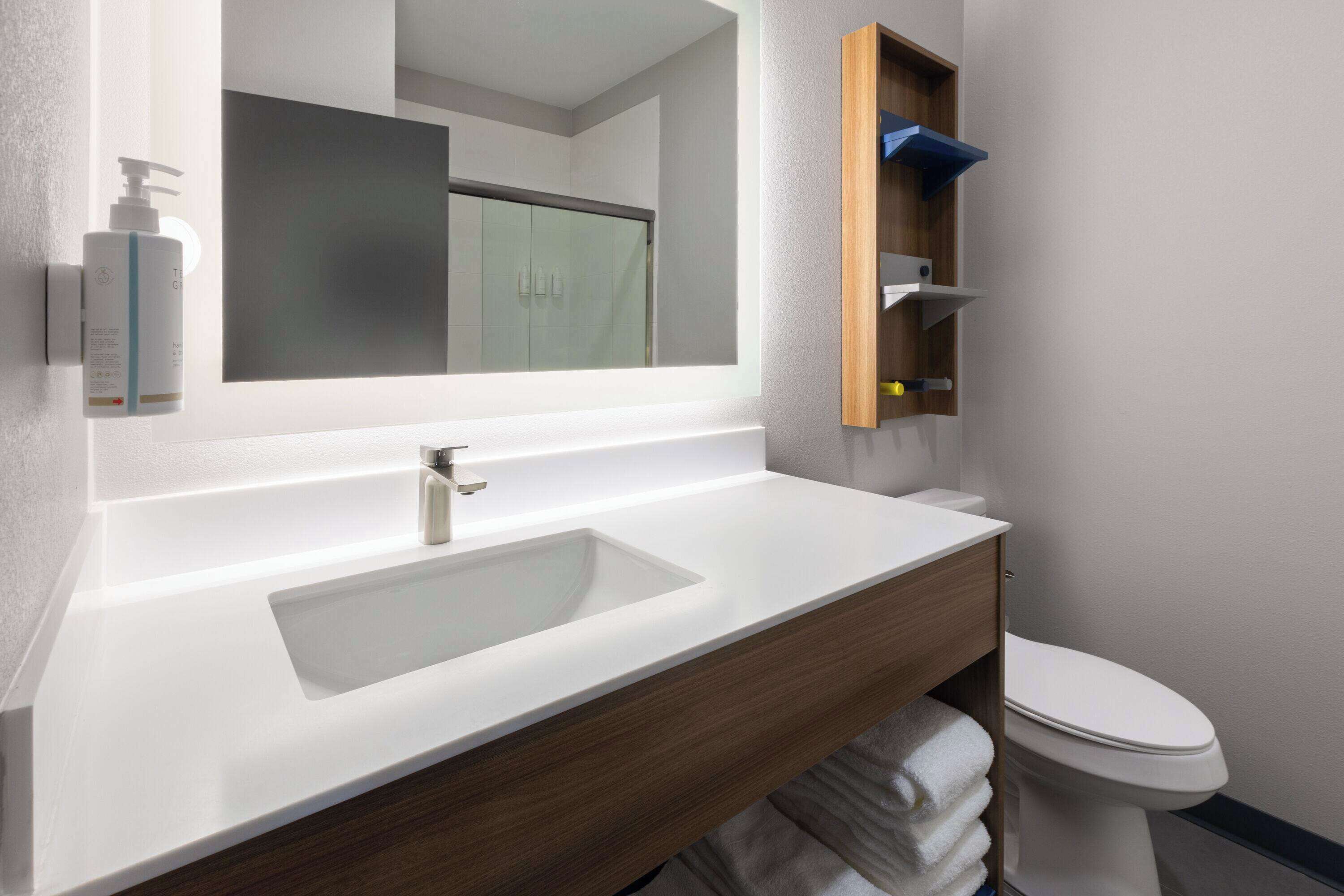 A modern bathroom with a white sink, wooden vanity, a mirror, and a toilet.
