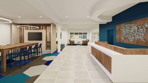 Eine moderne Hotellobby mit einer Rezeption, einem großen Bildschirm und einer Sitzecke mit Stühlen und einem Tisch.