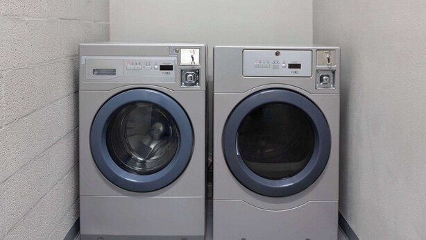 Deux machines à laver à chargement frontal sont placées dans un coin d’une pièce dont le sol est carrelé et dont un des murs est uni.