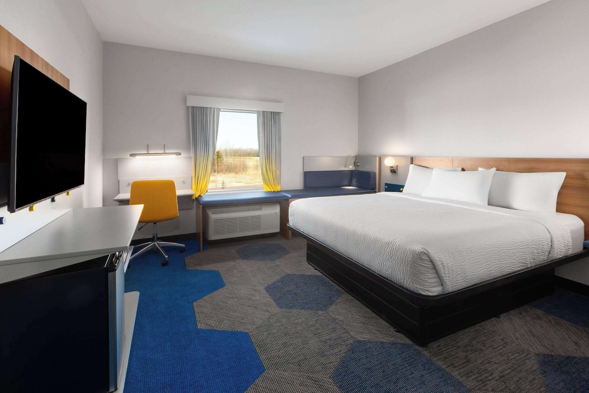 Une chambre d’hôtel équipée d’un lit, d’un bureau, d’une chaise, d’une télévision et d’une fenêtre avec des rideaux.