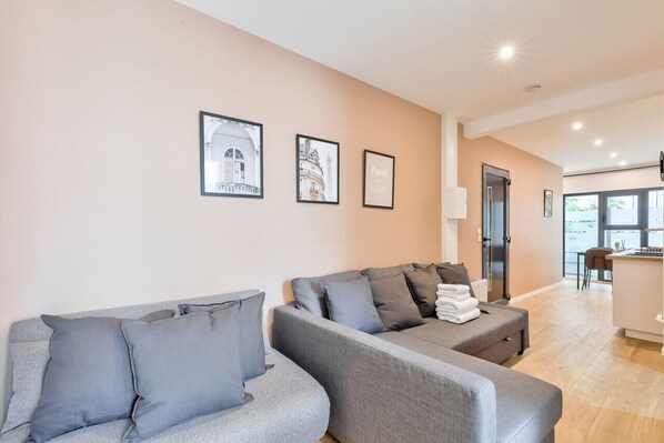 A modern living room with a grey sofa set, a small table with a lamp, and framed pictures on the wall.