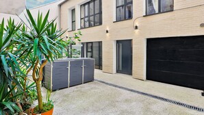 A modern building with a garage door, potted plants, and a concrete ground.