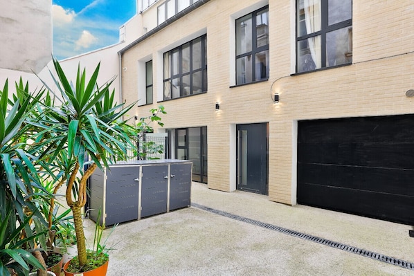 A modern building with a garage door, potted plants, and a concrete ground.