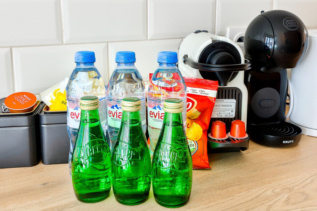 Una encimera de cocina con diversos objetos, incluyendo botellas de Evian, una cafetera y un hervidor eléctrico Krups.