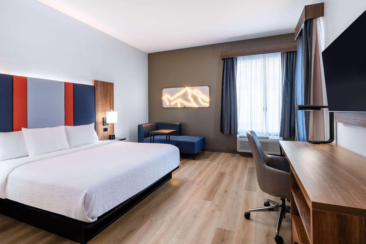 A hotel room with a bed, desk, chair, and a TV.