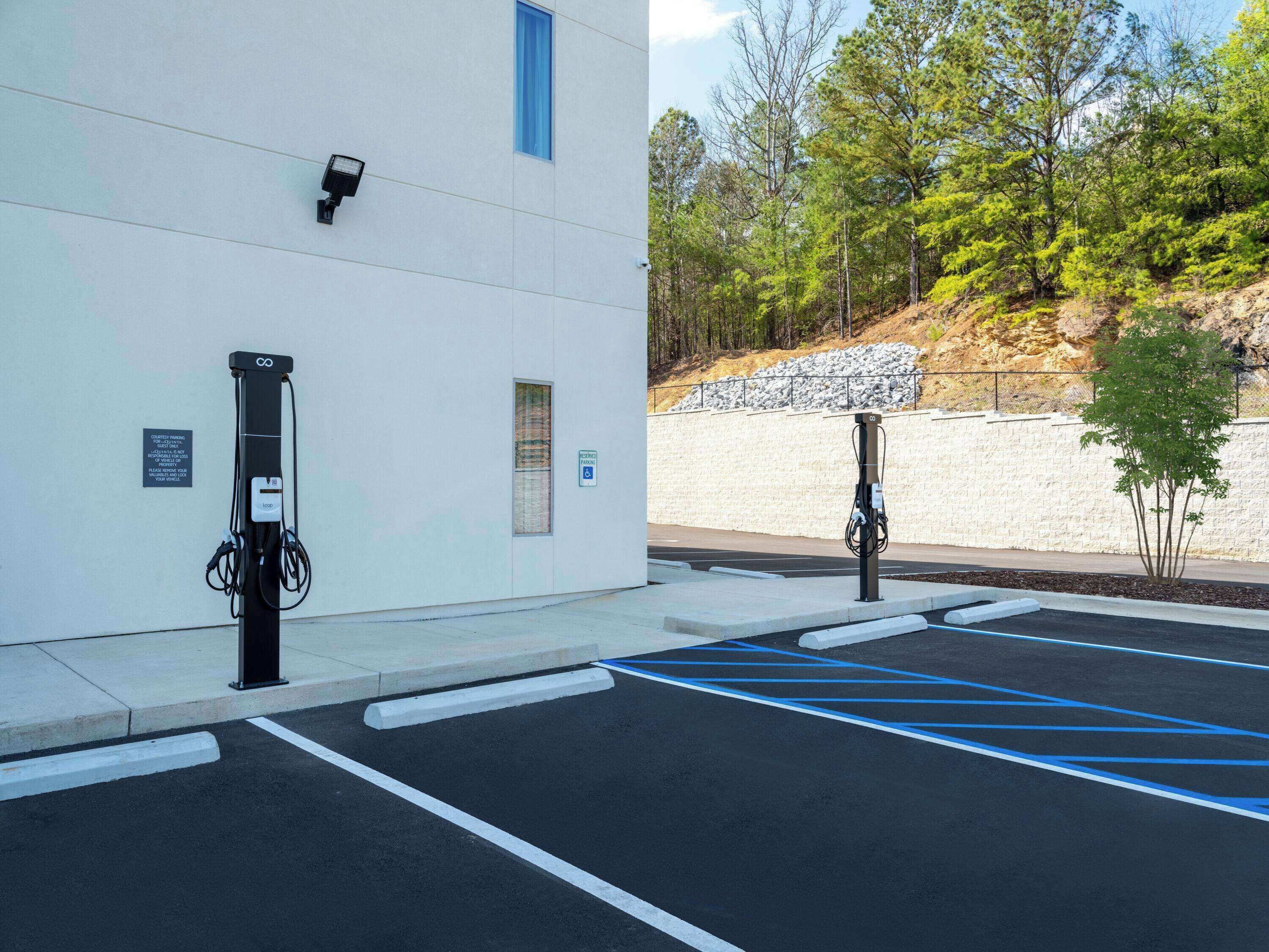 A parking area with electric vehicle charging stations, a building with a security camera, and a sign indicating handicapped parking.
