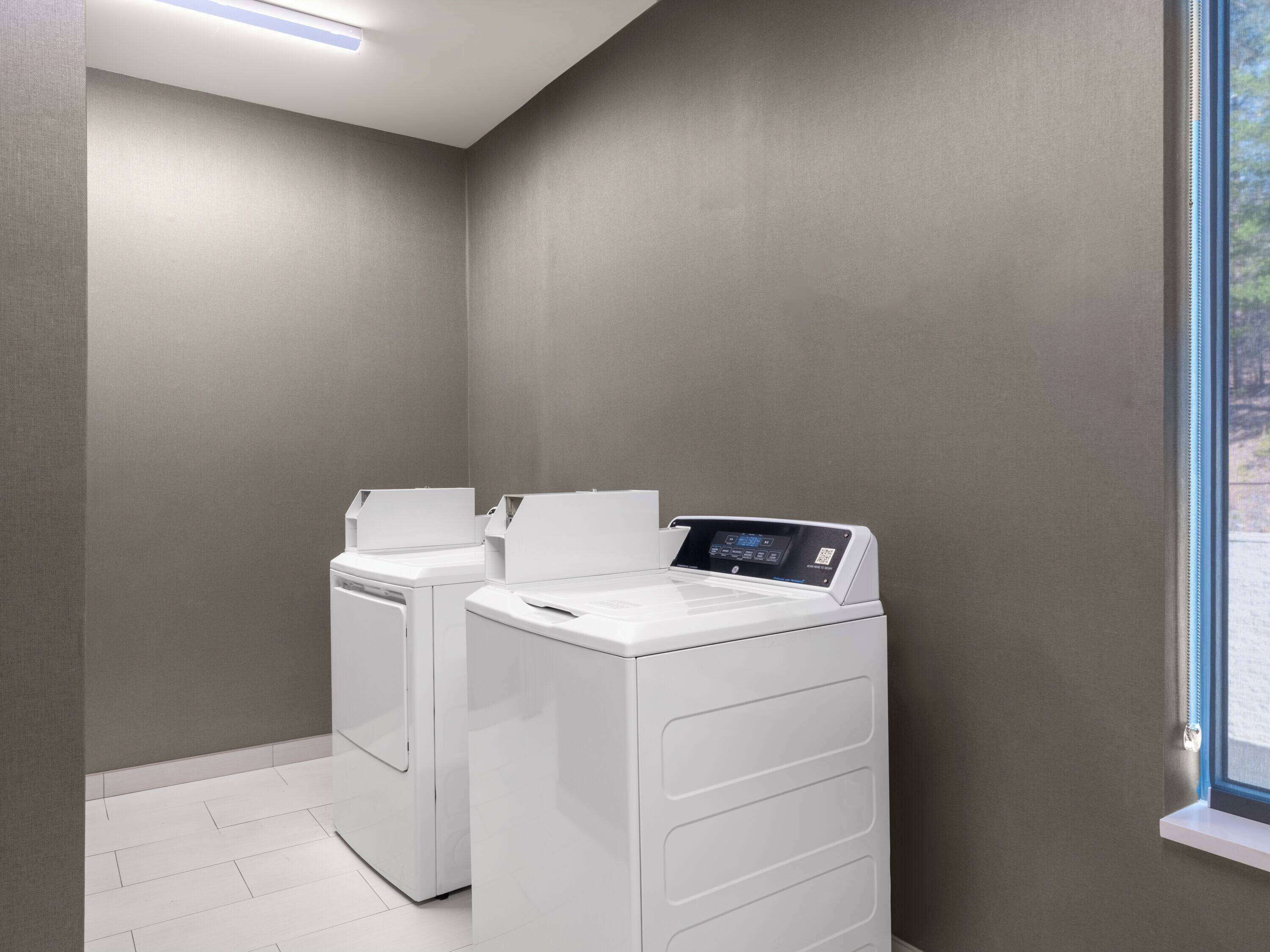 A laundry room with two white front-loading washing machines and a window.