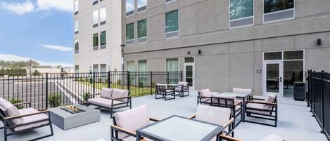 An outdoor patio with seating and tables, a building with multiple windows, and a clear sky.