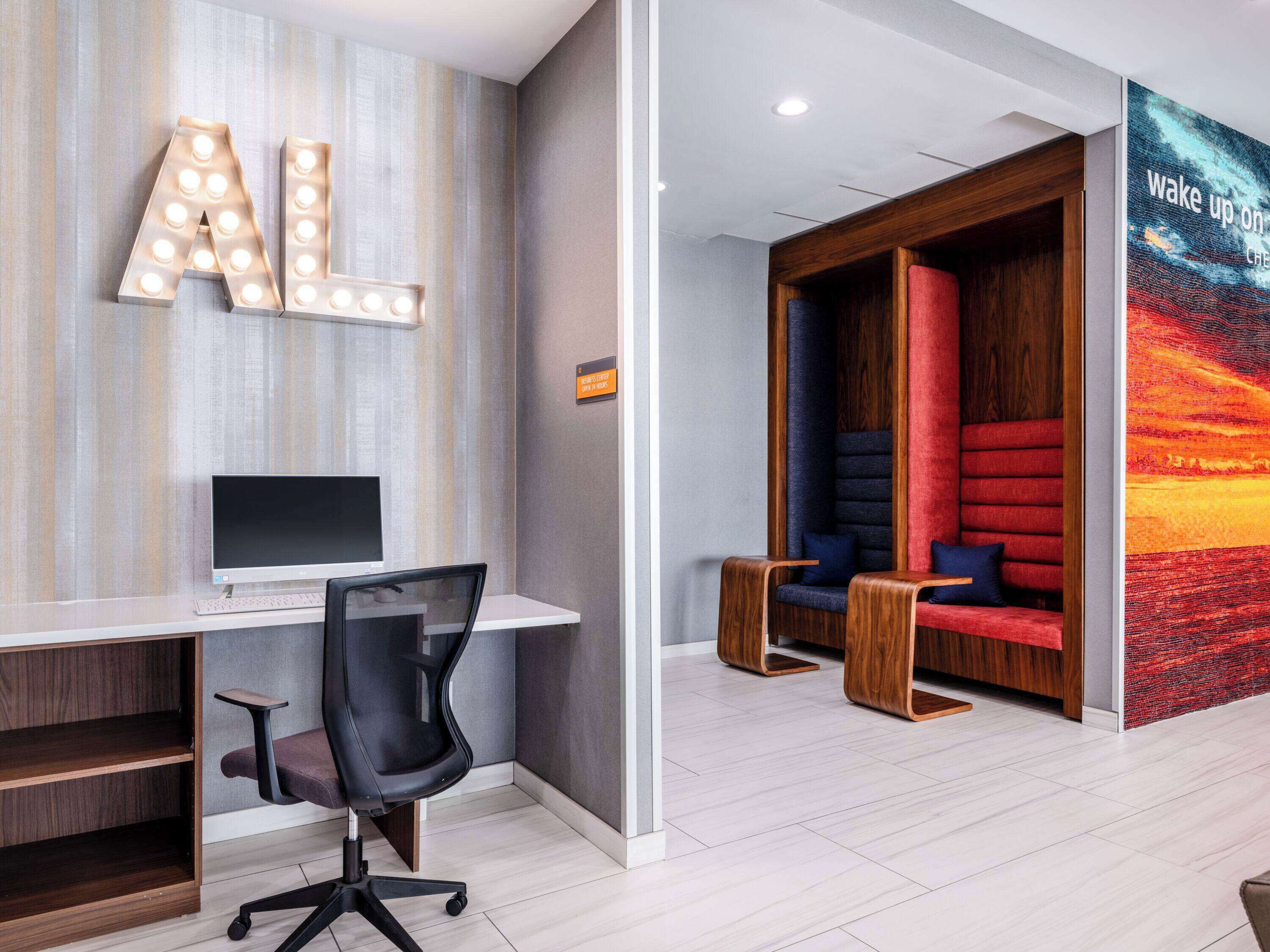 A modern office space with a desk, computer, and office chair. There is a wall with illuminated letters and a sign indicating a room for meetings.