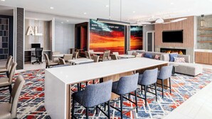 A modern lounge area with a long table, bar stools, and a fireplace. - La Quinta by Wyndham Chelsea Birmingham (Chelsea)
