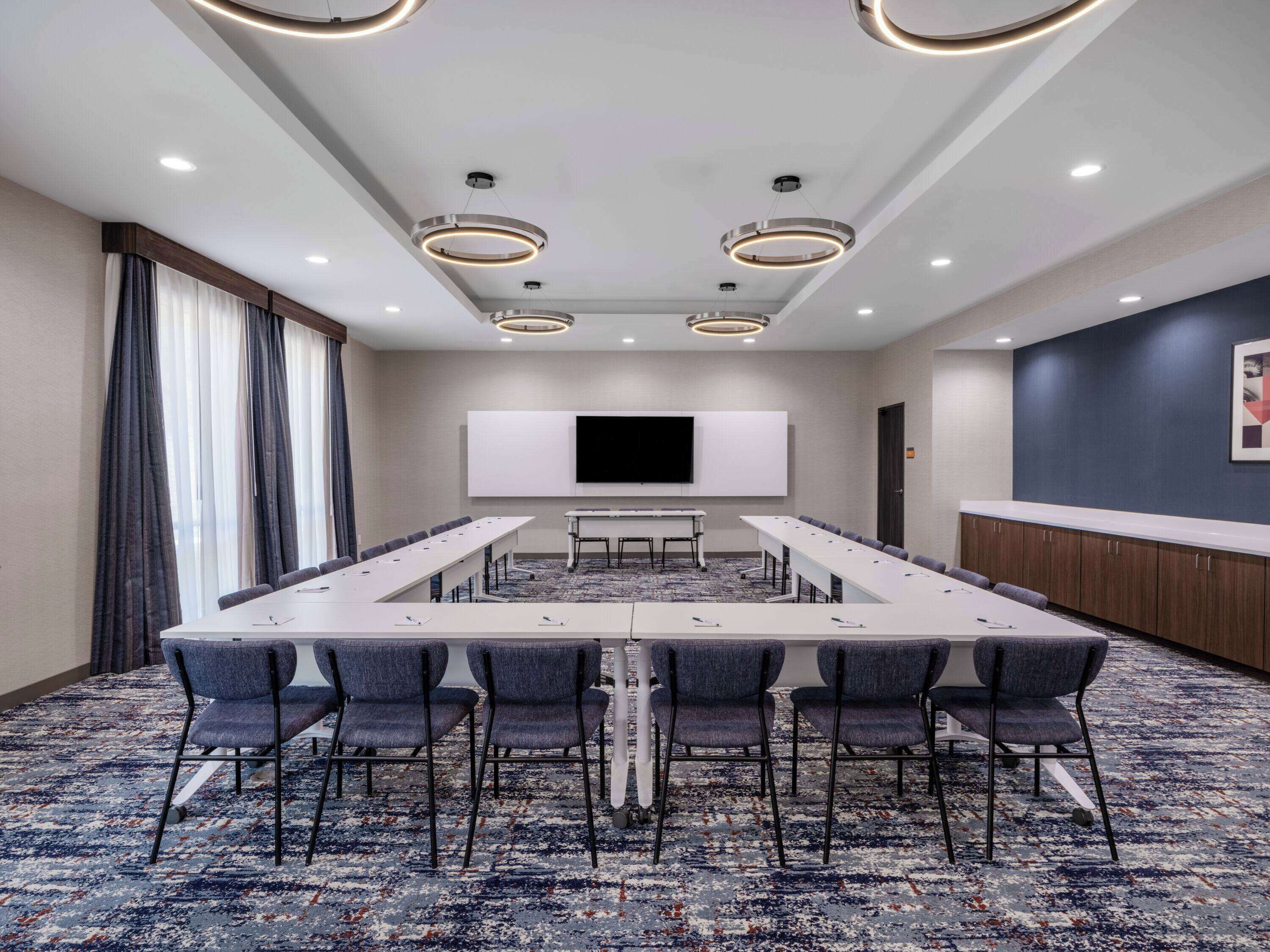 Une salle de conférence avec une longue table, des chaises, un grand écran et un sol recouvert de moquette.