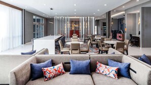 A modern hotel lobby with a long reception desk, multiple seating areas, and a large window providing natural light. - La Quinta by Wyndham Chelsea Birmingham (Chelsea)