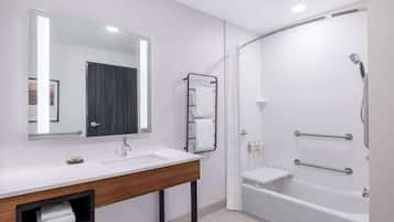 A modern bathroom with a white sink, a large mirror, a towel rack, and a walk-in shower with grab bars.