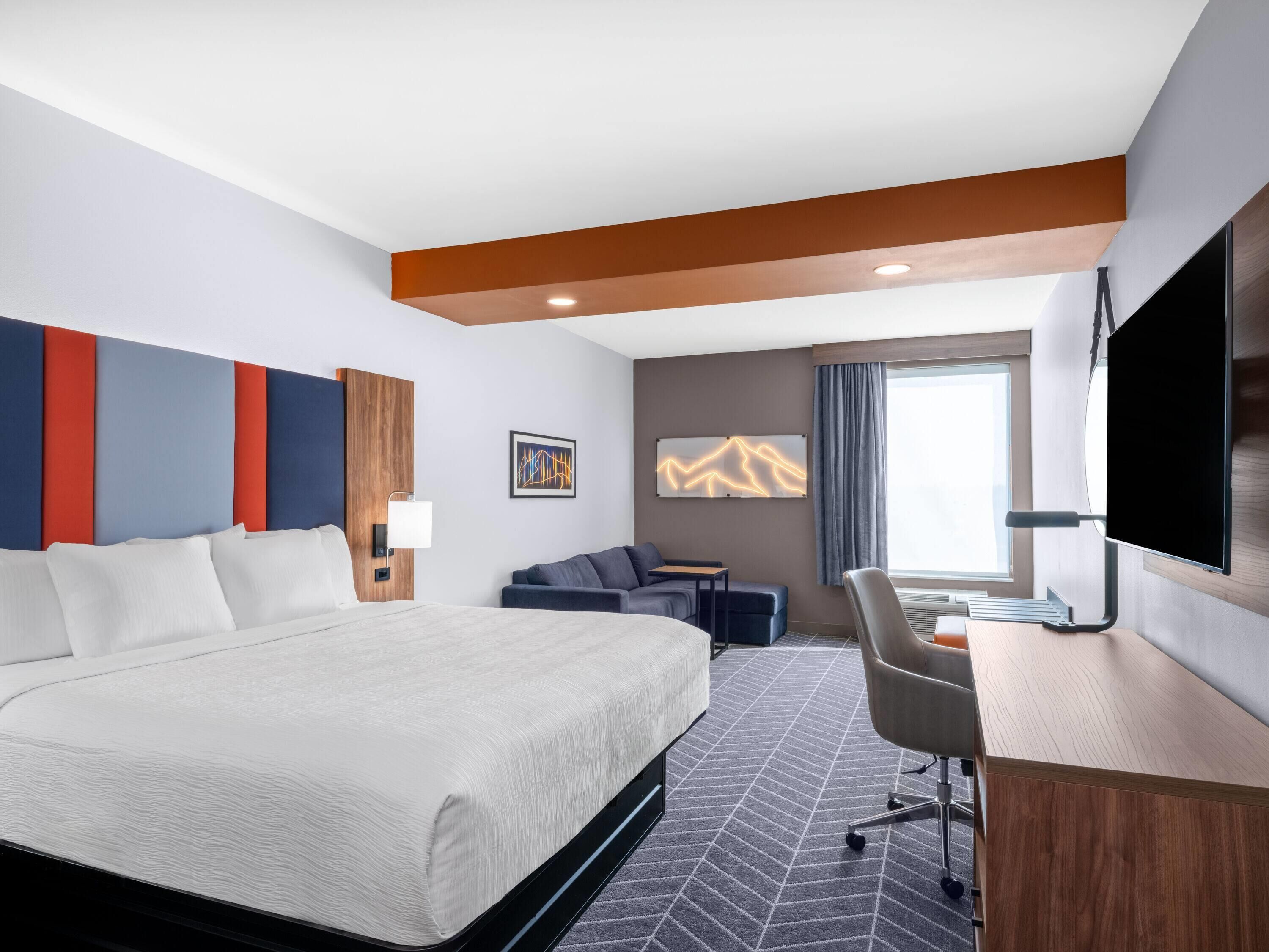 Una habitación de hotel moderna con una cama grande, un escritorio, una silla, un sofá y un televisor.