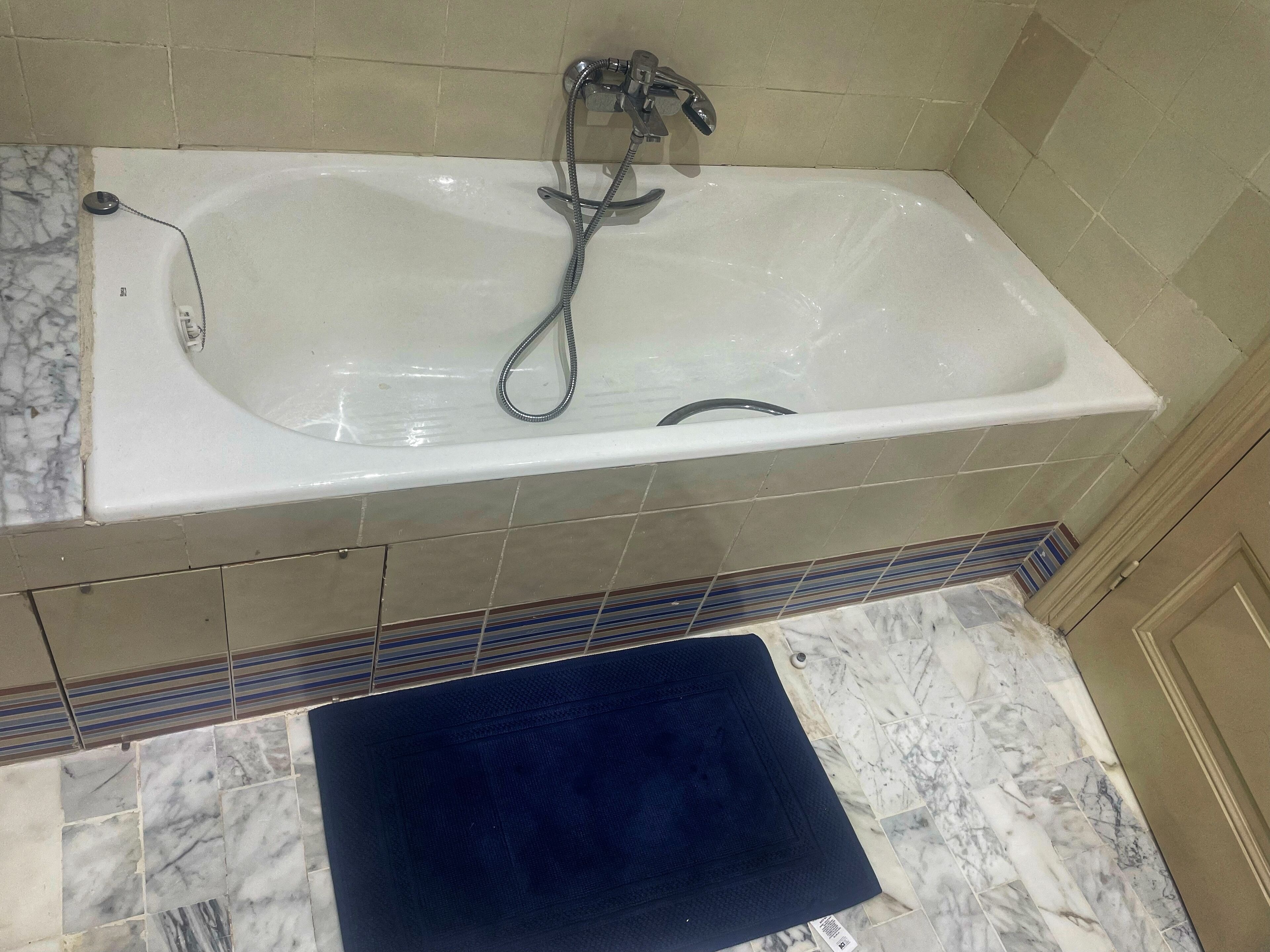 Een badkamer met een witte badkuip, een douchekop en een betegelde vloer.