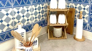 A kitchen corner with a wooden utensil holder, a hanging plant, and a shelf with white containers.