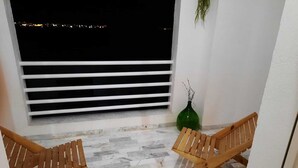 A balcony with two wooden chairs, a green vase, and a window with horizontal blinds.