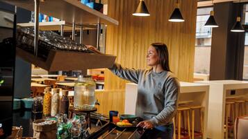 Una persona operando una cafetera en un café moderno con interior de madera y taburetes de bar.