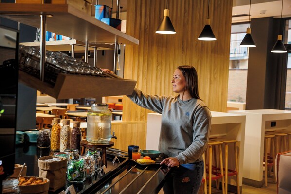 A person operating a coffee machine in a modern cafe with a wooden interior and bar stools. - ibis budget Logroño Centro (Logroño)