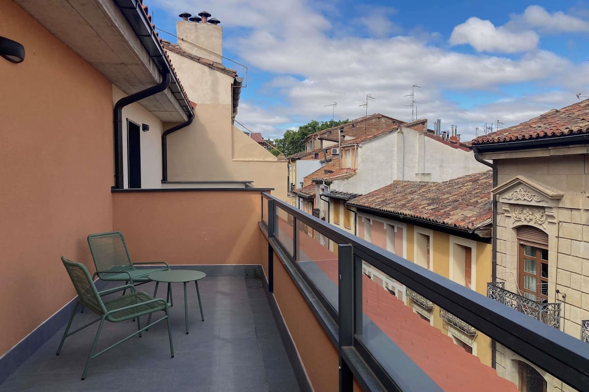 A balcony with a table and chairs, a railing, and a view of neighboring buildings.