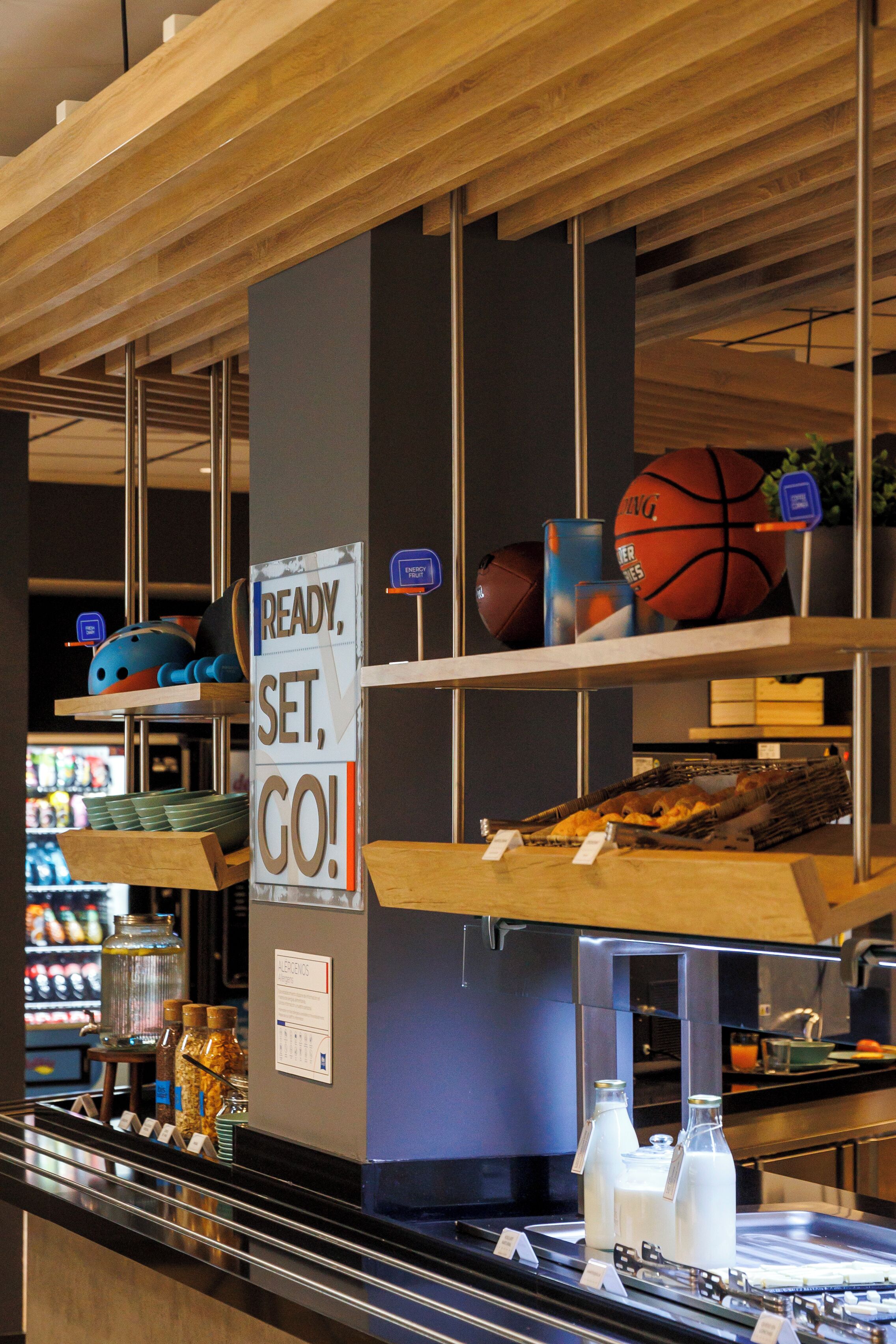 A sports equipment section with a sign that reads "READY, SET, GO!" and shelves with various sports balls and equipment.