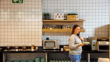 A kitchen area with a woman holding a plate of food, a microwave, a toaster, and shelves with jars and mugs.