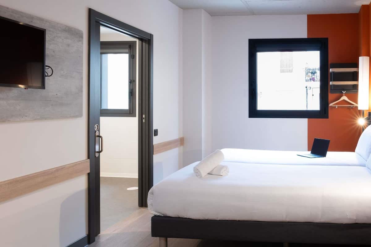 A hotel room with a bed, a laptop, a towel, a door, and a window.
