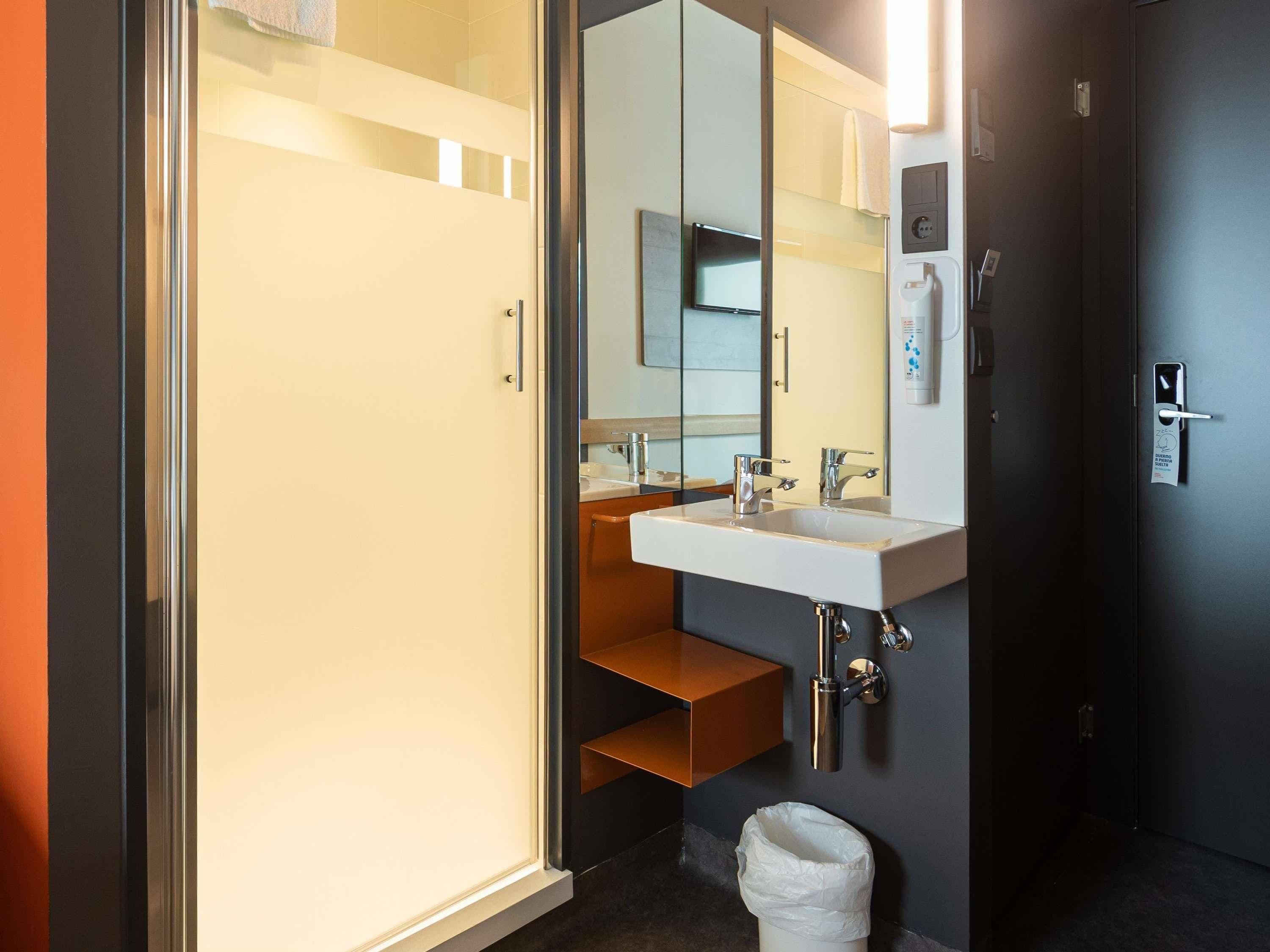 A modern bathroom with a glass shower enclosure, a white sink with a mirror, and a towel rack.