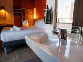 A hotel room with a bed, a white sink, and a mirror.