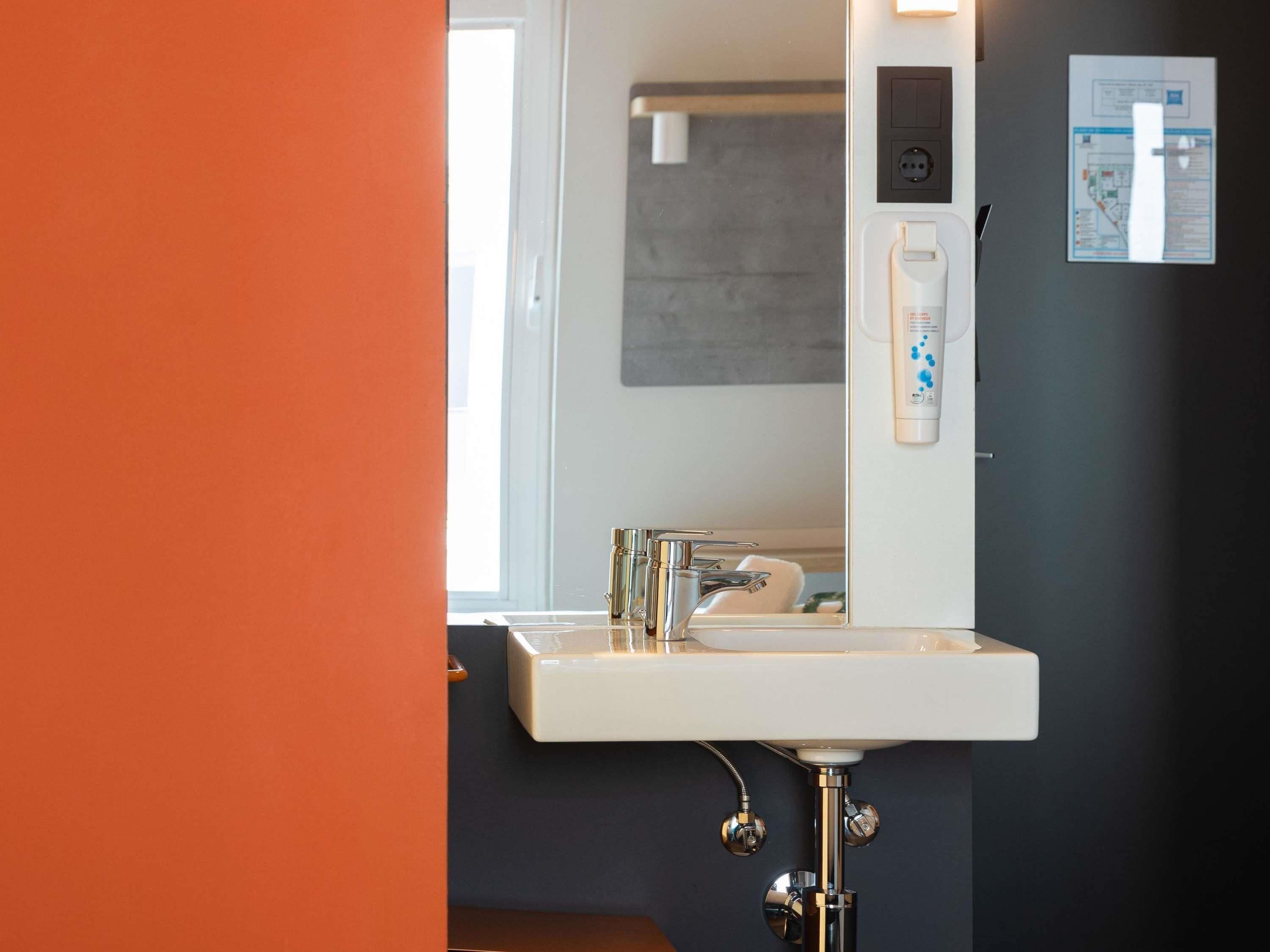 Un baño moderno con lavamanos blanco, accesorios de cromo y un espejo.