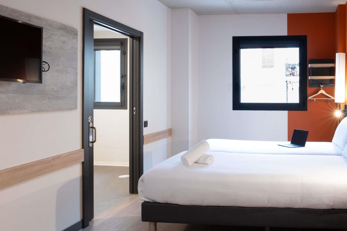 A hotel room with a bed, a laptop, a towel, a door, and a window.