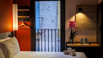 Habitación de hotel con cama, mesita de noche con lámpara, orquídea en maceta y vistas al exterior.