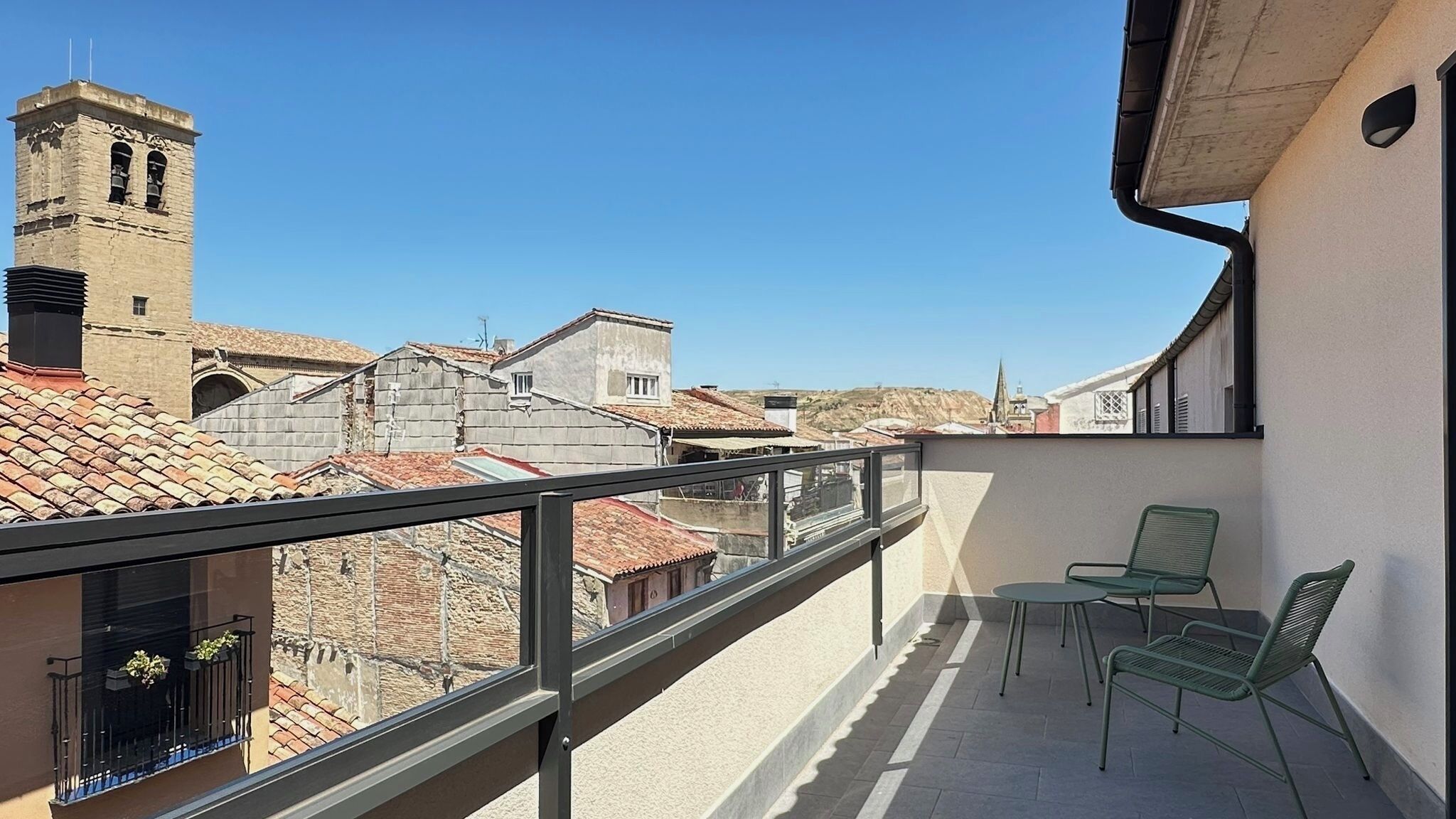 Ein Balkon mit einem Metallgeländer, zwei grünen Stühlen und einem Tisch.